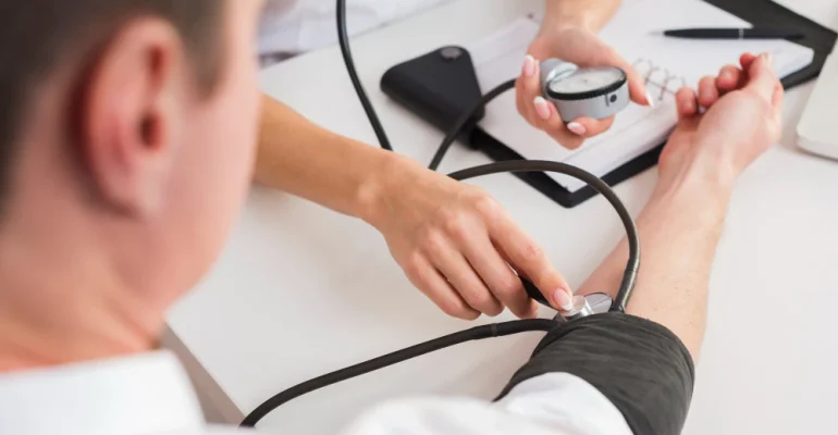 Healthcare provider measuring a patient’s blood pressure with a manual cuff and stethoscope during a routine medical exam.